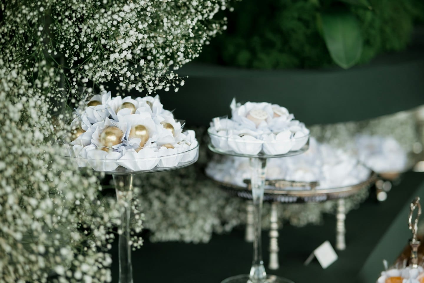 Dulces elegantes para fiestas dispuestos en pedestales de vidrio con flores blancas.